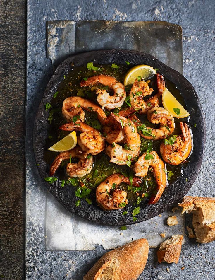 a pan filled with shrimp and lemon wedges on top of a table next to bread