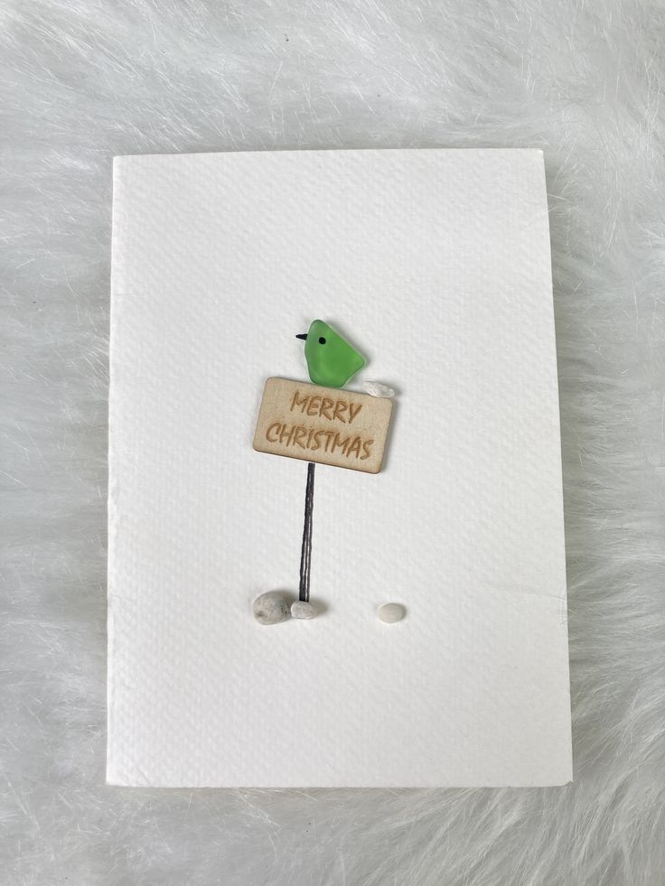 a white card with a green bird on it and a merry christmas sign in the middle