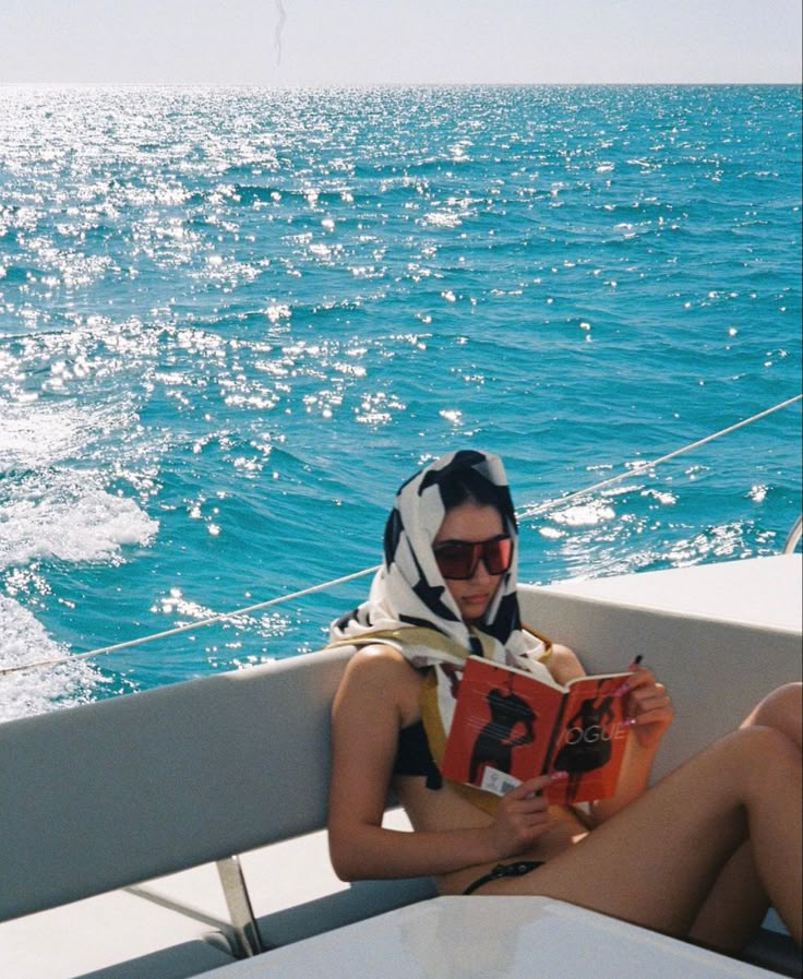 a woman sitting on the back of a boat while reading a book in her lap