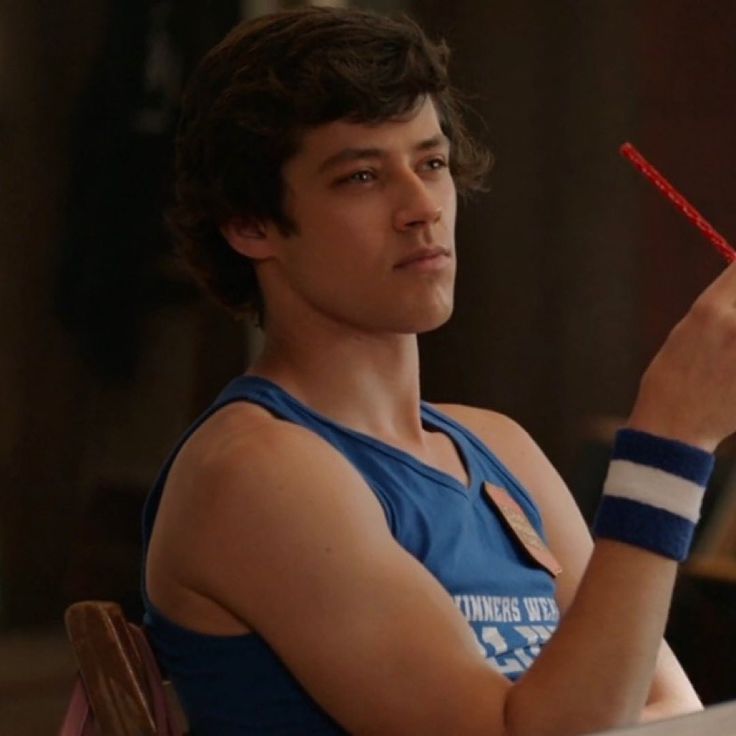 a young man sitting at a table with a red object in his hand and looking off to the side