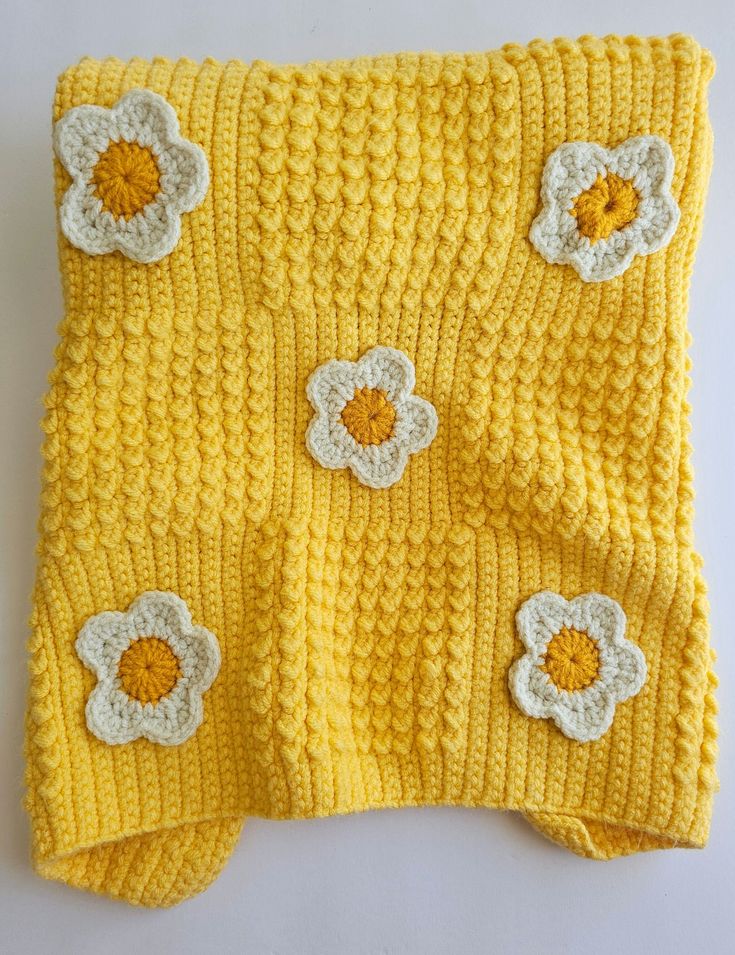 a crocheted yellow blanket with white flowers on the front and back, sitting on top of a table