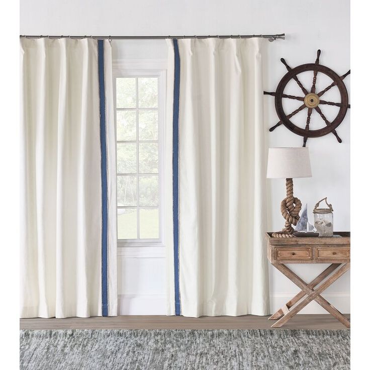 a white curtain with blue stripes hanging in front of a window next to a wooden table