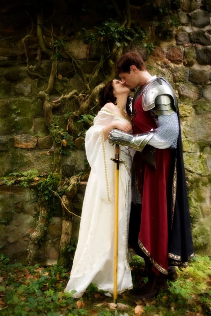 a man and woman dressed in medieval costumes kissing each other while standing next to a stone wall