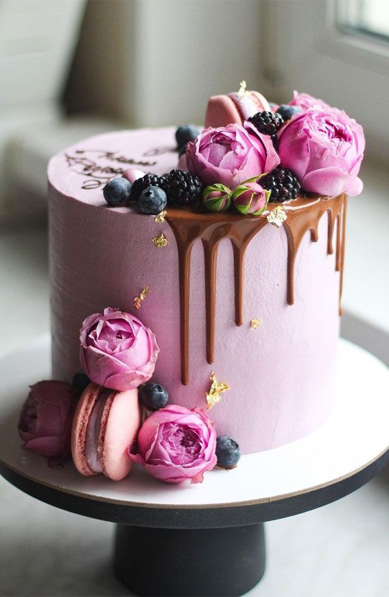 a pink cake with chocolate icing and flowers on top is sitting on a table