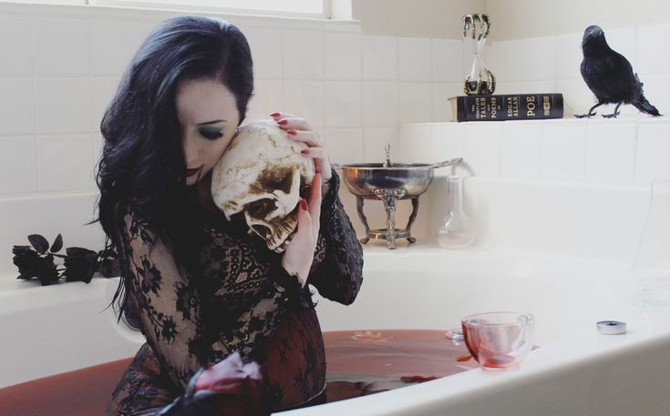 a woman sitting in a bathtub holding a skull