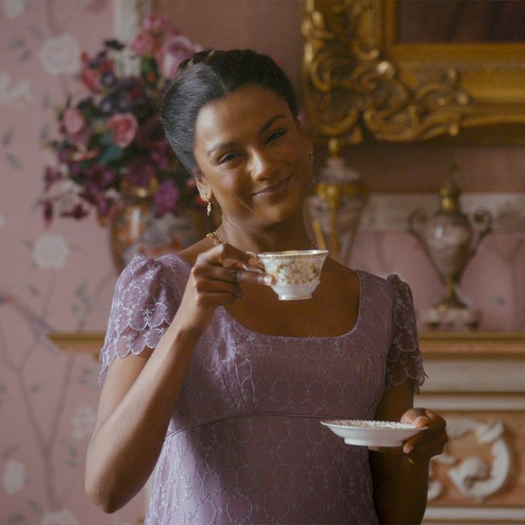 a woman in a purple dress holding a white cup and saucer while smiling at the camera