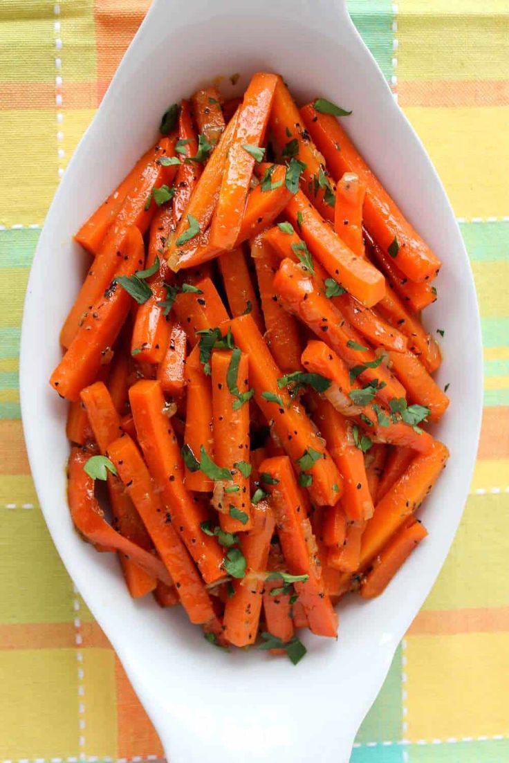 a white bowl filled with sliced carrots on top of a colorful table cloth next to a spoon