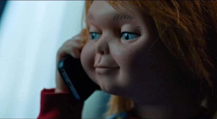 a close up of a doll talking on a cell phone with red hair and blue eyes