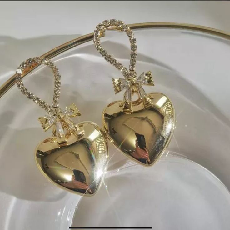 This Is A Very Beautiful Pair Of Gold Plated Metal Heart Dangle Earrings . They Have A Bow Made Of Baguette Cz Stones And The Top Of Earrings Have Pave Cz Stones . The Length Is 3.8 Inches And The Hearts Are A Puffed Heart Design . Gold Heart-shaped Earrings With Rhinestones, Gold Rhinestone Heart Earrings, Gold Heart Earrings With Rhinestones For Valentine's Day, Glamorous Heart Earrings With Rhinestones As Gift, Elegant Heart Pendant Earrings For Party, Elegant Rhinestone Heart Earrings As Gift, Glamorous Rhinestone Heart Earrings As Gift, Glamorous Rhinestone Heart Earrings For Gift, Elegant Heart Earrings For Party