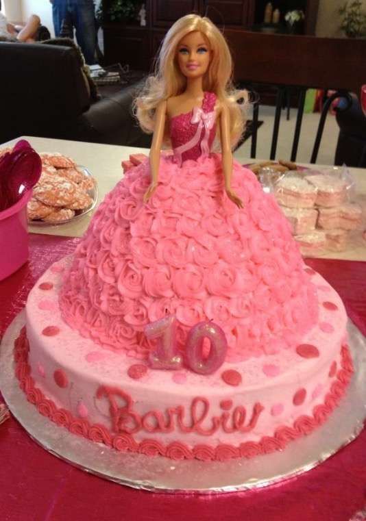 a barbie doll cake with pink frosting and roses on it, sitting on a table