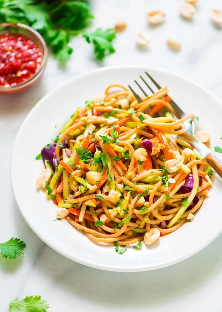 a white plate topped with noodles and vegetables next to a bowl of sauce on the side