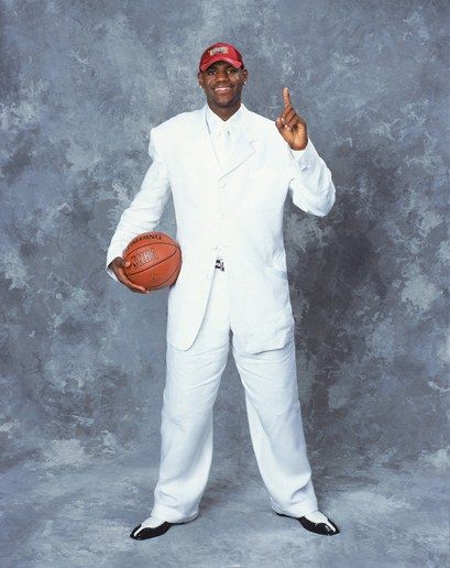 a man in a white suit holding a basketball and giving the peace sign with his right hand