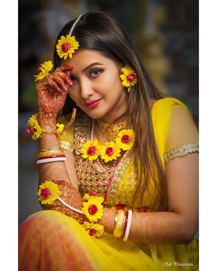 a woman in yellow dress with flowers on her head and hands behind her head, posing for the camera