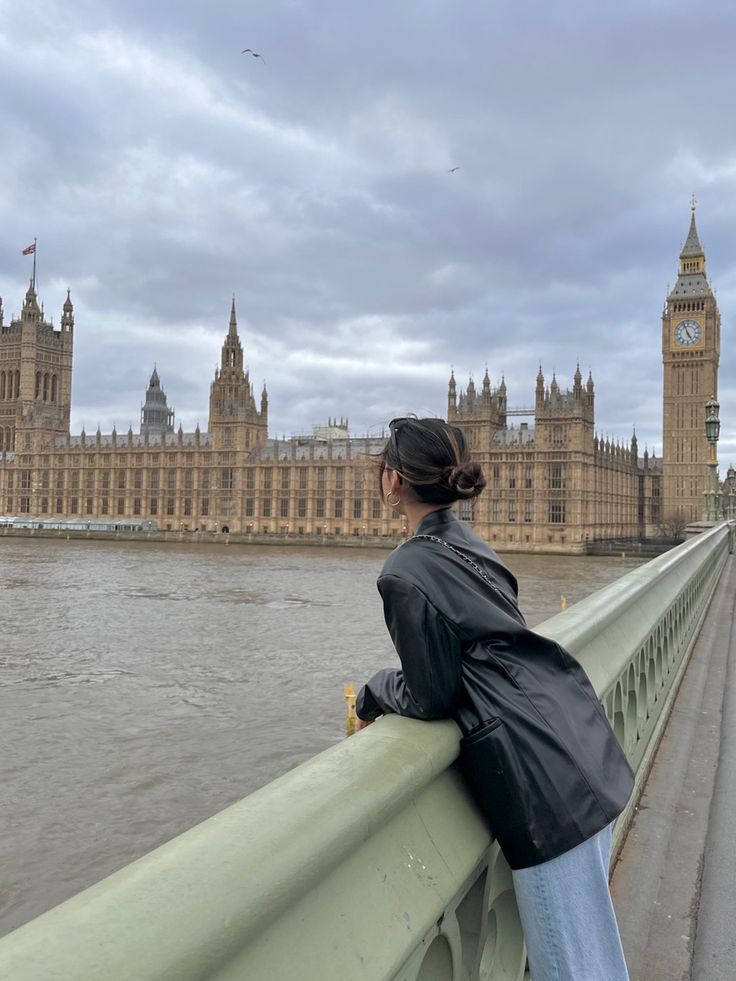 a woman standing on the edge of a bridge looking at big ben in london, england