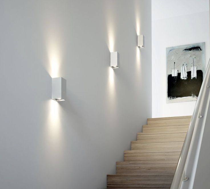 three lights are on the wall next to some stairs in a room with white walls