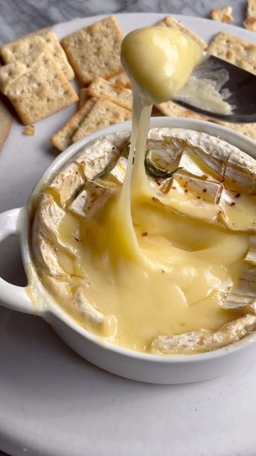 a spoon is pouring cheese into a bowl with crackers and crackers on the side