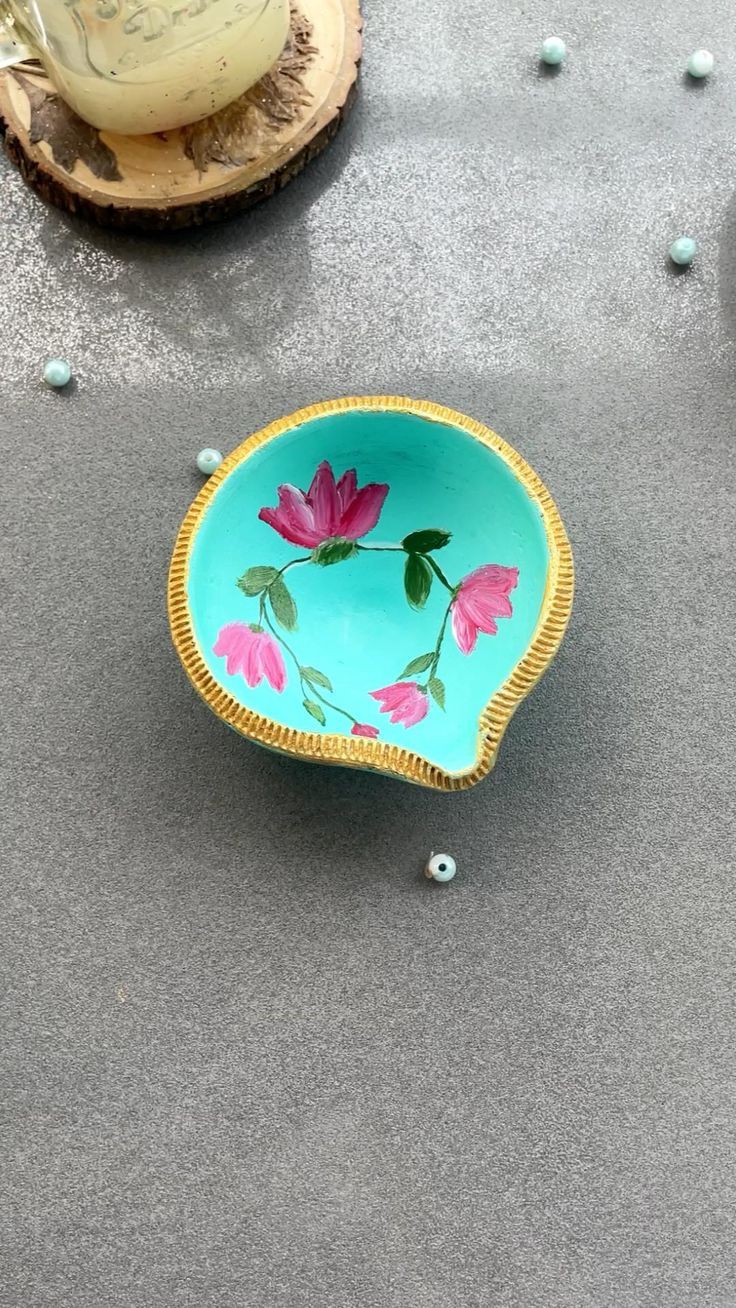 a blue bowl with pink flowers painted on it sitting on the ground next to other items