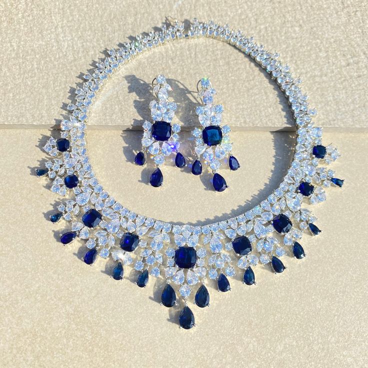 Sapphire Necklace features blue diamonds and navy blue stones in a teardrop design. Crafted with cubic zirconia, it's a modern, contemporary piece perfect for an Indian bride. An elegant and timeless wedding gift for her. *𝐏𝐑𝐎𝐃𝐔𝐂𝐓 𝐃𝐄𝐓𝐀𝐈𝐋* * 𝐌𝐚𝐭𝐞𝐫𝐢𝐚𝐥: Brass * 𝐏𝐥𝐚𝐭𝐢𝐧𝐠: White Rhodium Plated * 𝐒𝐭𝐨𝐧𝐞: AAA-quality CZ Diamond & Sapphire. *𝐃𝐈𝐌𝐄𝐍𝐒𝐈𝐎𝐍𝐒* *𝐍𝐞𝐜𝐤𝐥𝐚𝐜𝐞* * 𝐖𝐞𝐢𝐠𝐡𝐭: 140 gm * 𝐋𝐞𝐧𝐠𝐭𝐡: 7.5 Inches *𝐄𝐚𝐫𝐫𝐢𝐧𝐠𝐬* * 𝐖𝐞𝐢𝐠𝐡𝐭: 16 gm e Blue Drop Jewelry With Diamond Accents, Blue Teardrop Pendant Jewelry With Diamond Accents, Blue Teardrop Pendant With Diamond Accents, Blue Teardrop Jewelry With Diamond Accents, Blue Teardrop-shaped Jewelry With Diamond Accents, Teardrop Sapphire Cubic Zirconia Jewelry, Teardrop Sapphire-colored Cubic Zirconia Jewelry, Pear-shaped Blue Diamond Jewelry, Blue Pear-shaped Diamond Jewelry