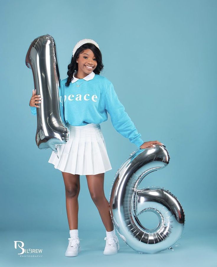 a woman in a blue sweater and white skirt holding a large silver number six balloon