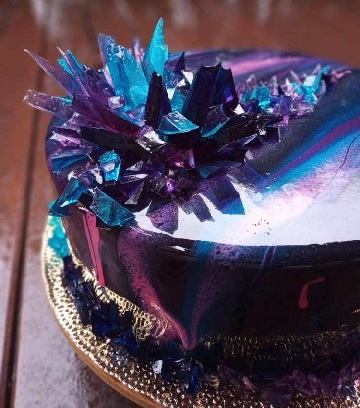 a cake with purple and blue frosting on a gold plate sitting on a wooden table