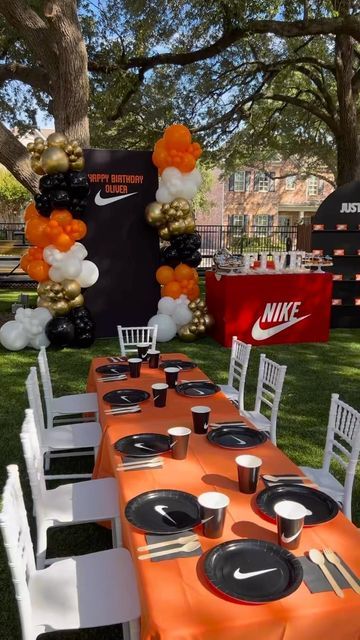 an orange and white table set up for a nike birthday party with balloons, plates, napkins and cups