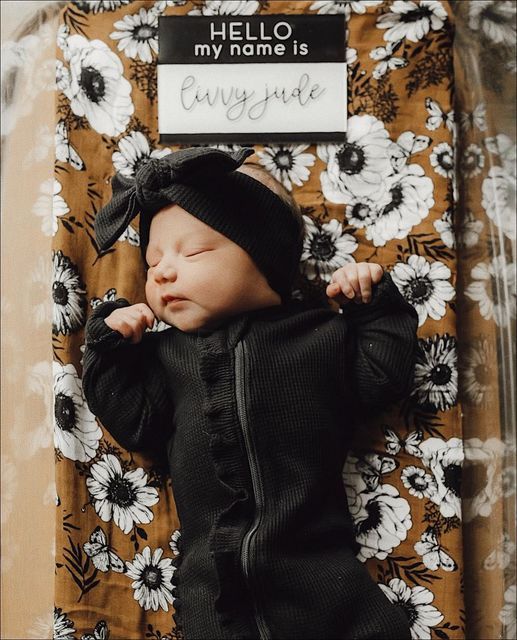 a baby is laying down wearing a black outfit and a beanie with the name hello my name is written on it