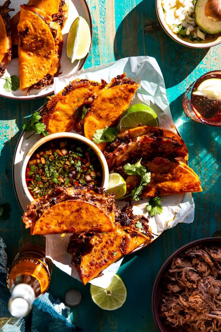 an overhead view of several plates of food on a blue wooden table with lime wedges