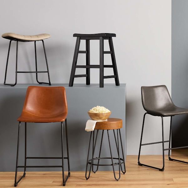 four different types of chairs and stools against a gray wall with wood flooring