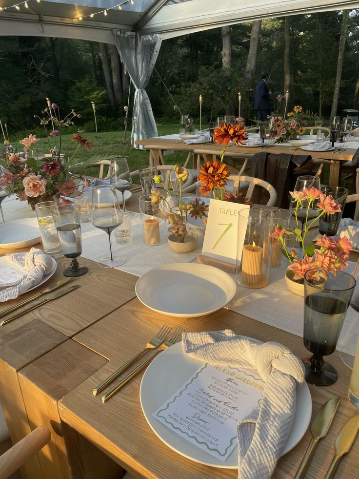 a table set with place settings and flowers in vases on the table for an outdoor dinner party