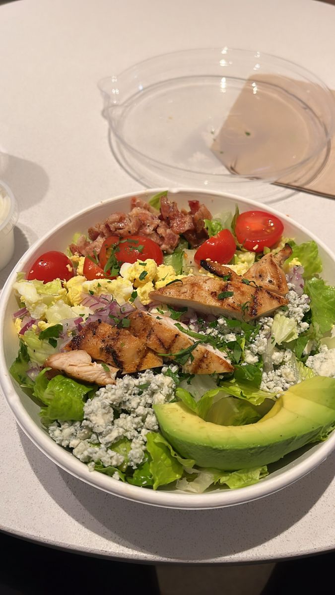 a salad with chicken, lettuce, tomatoes and avocado in a bowl