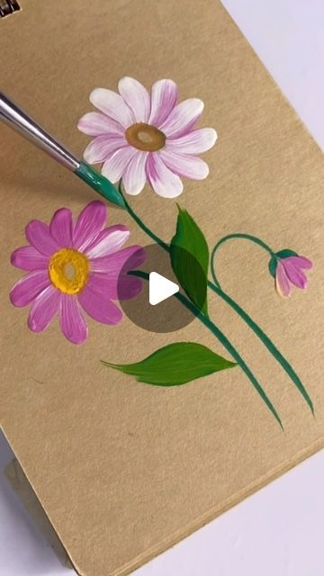 someone is painting flowers on a piece of brown paper with a paintbrush in their hand