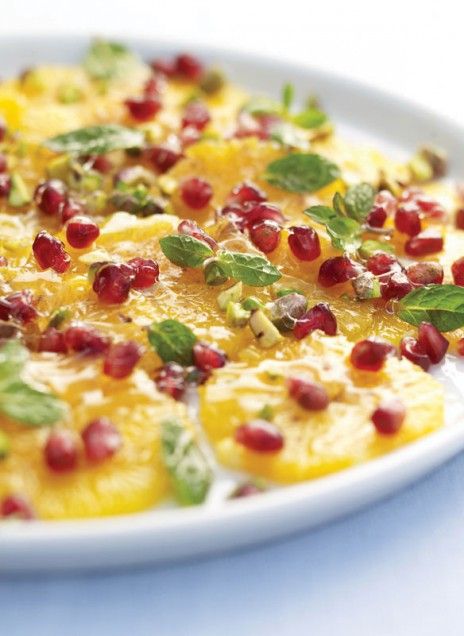 a white plate topped with oranges and pomegranate on top of green leaves