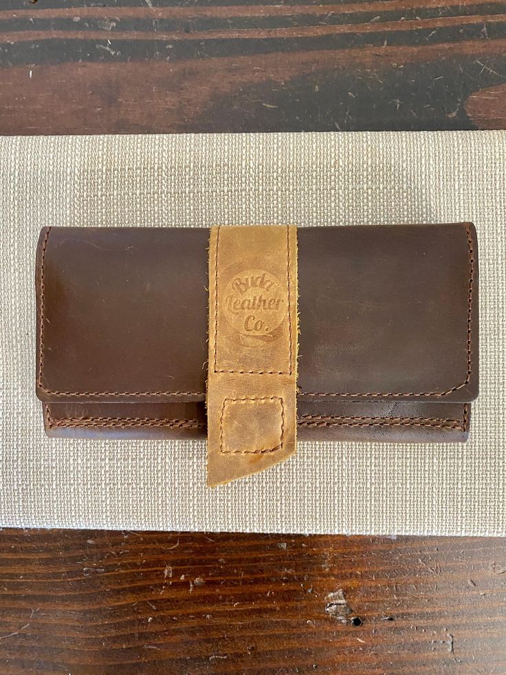 Keep your essentials chic and secure with our Belle Wallet. Crafted from structured brown leather with a light leather contrast, this wallet features a convenient magnetic snap closure and our signature logo stamp. The perfect blend of fashion and functionality! Fits a phone and card slots. 4" x 8" Buda Leather Co products are handmade in Buda, Texas Please note that each piece is one of a kind with natural leather and natural imperfections. Cognac Trifold Wallet With Card Slots For Everyday Use, Leather Trifold Wallet With Magnetic Closure For Travel, Brown Wallets With Card Slots For Everyday Use, Travel Wallets With Leather Lining In Brown, Leather Travel Wallet In Cognac, Brown Leather-lined Wallet For Travel, Travel Wallet With Brown Leather Lining, Travel Wallet In Cognac With Leather Lining, Everyday Brown Wallets With Card Slots