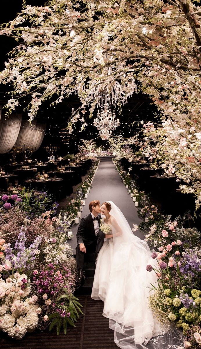 a bride and groom are kissing in front of an archway with flowers all around them