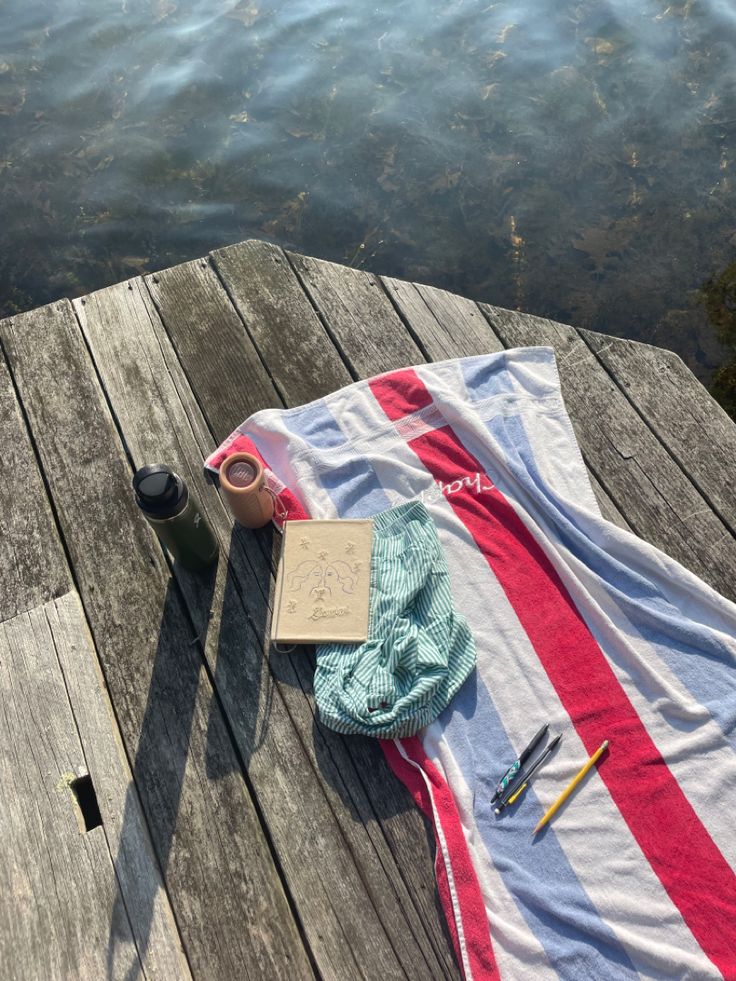 a towel, cup and book on a wooden dock by the water