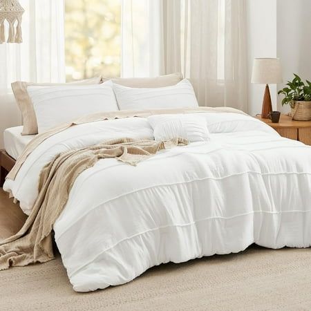 a bed with white linens and pillows in a room next to a lamp on a table