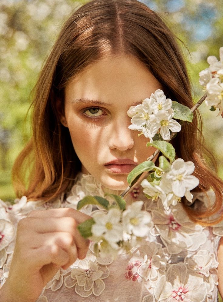 a woman with flowers on her face holding onto the leaves of a flowery branch