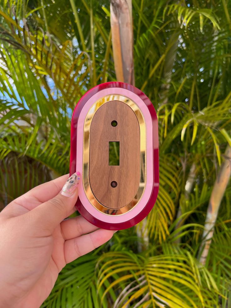 a person holding up a wooden object in front of some trees and palm tree branches