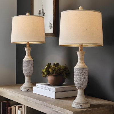 two lamps sitting on top of a wooden table next to a mirror and bookcase