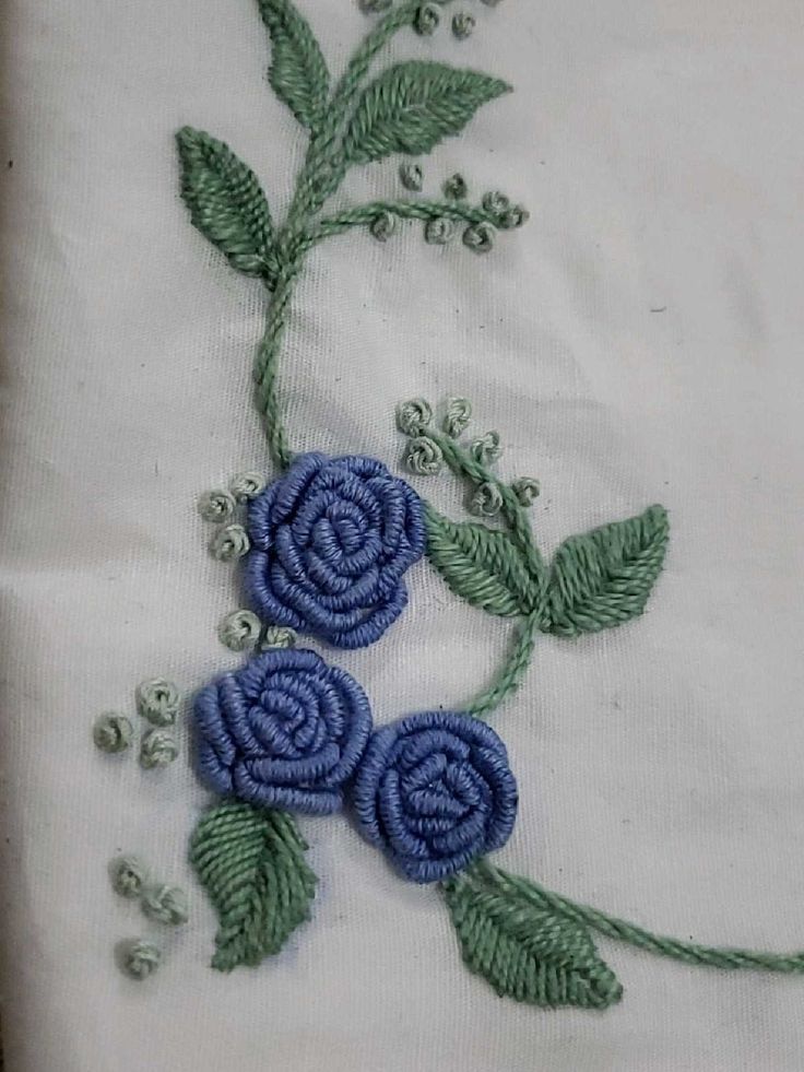 two blue flowers on white fabric with green leaves and beadwork around the edges