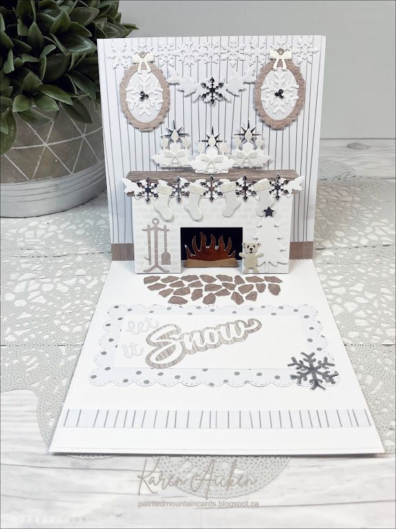 a white card with a fireplace and snowflakes on the front, sitting next to a potted plant