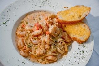 a white plate topped with pasta and shrimp next to two slices of toasted bread