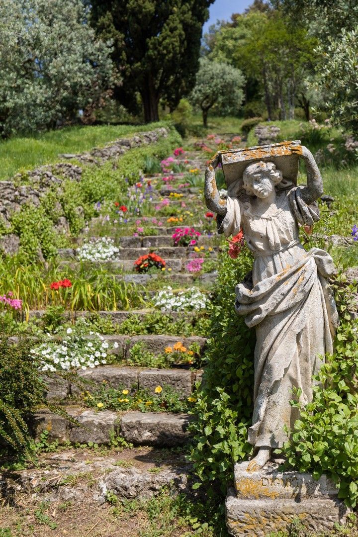 a statue in the middle of a garden with steps leading up to it and flowers growing all around