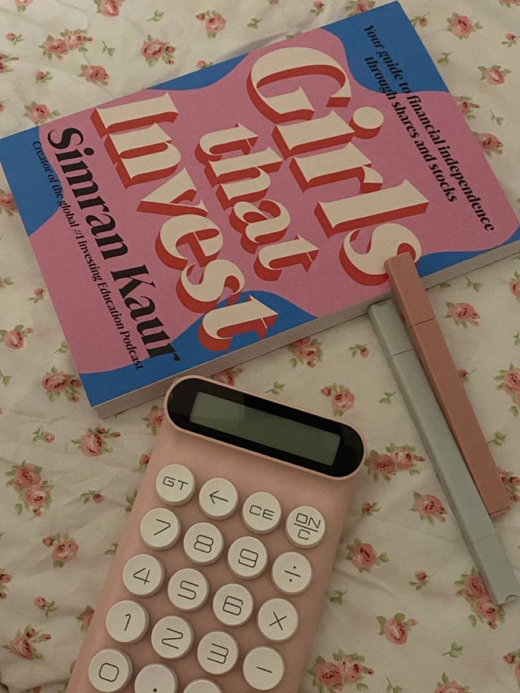 a pink calculator sitting on top of a bed next to a book