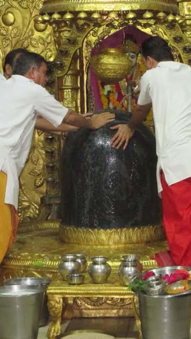 two men in white shirts and red pants standing next to a gold statue with bowls on it