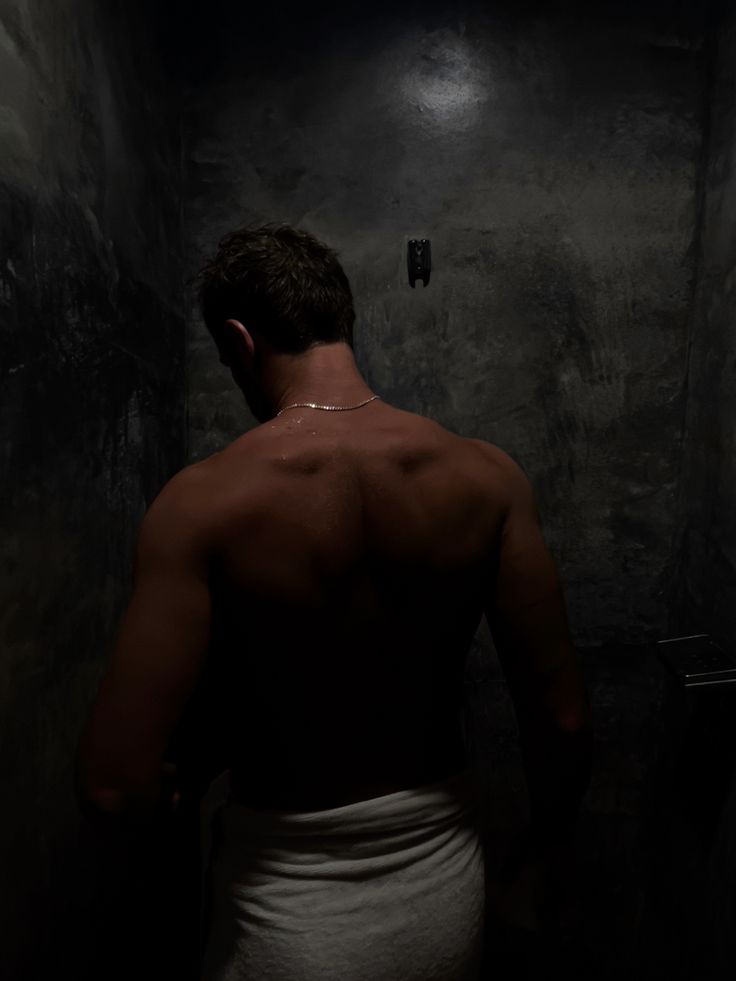 a man in a towel standing in a dark room with his back turned to the camera