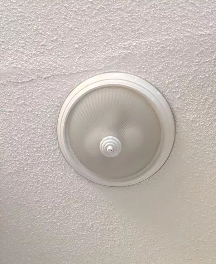 a ceiling light that is on in a room with white walls and plaster paint covering it