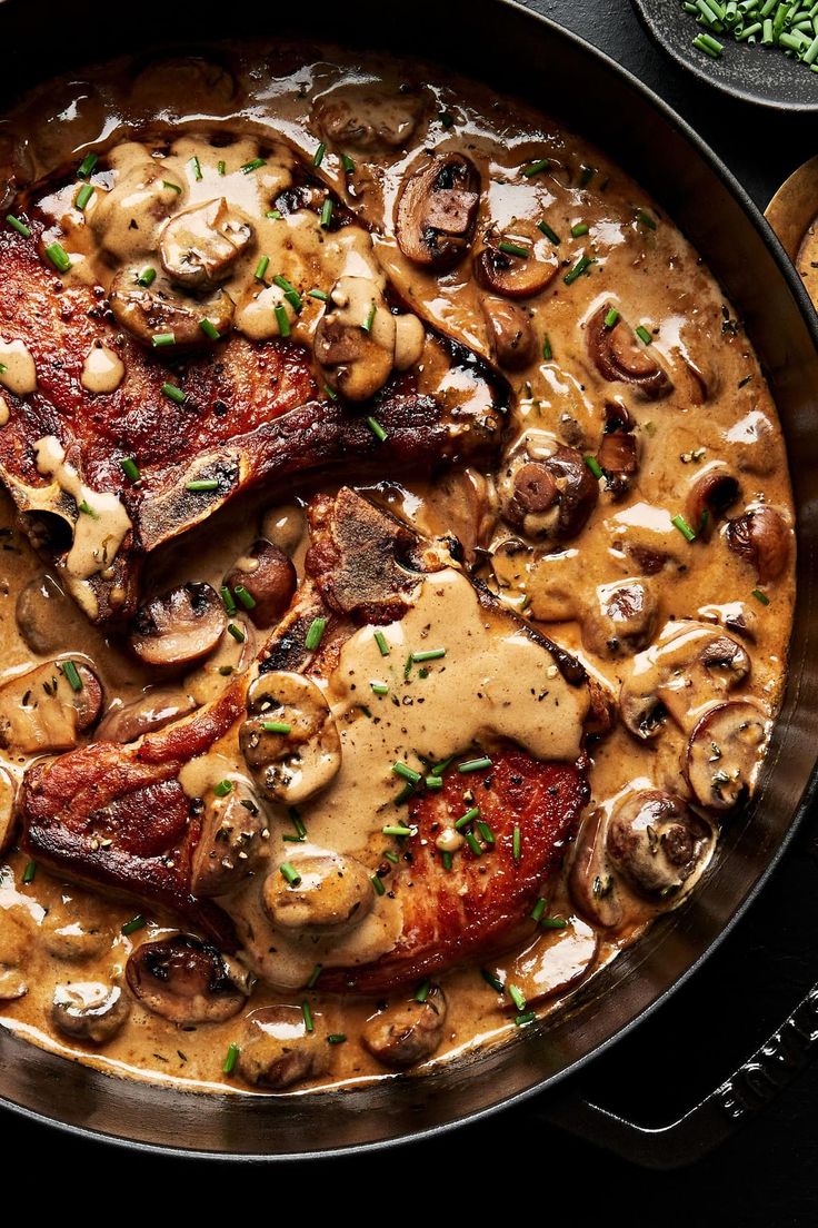 a pan filled with meat, mushrooms and gravy on top of a table