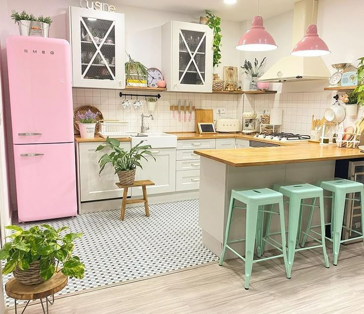 a pink refrigerator in a kitchen next to three stools and a table with potted plants on it