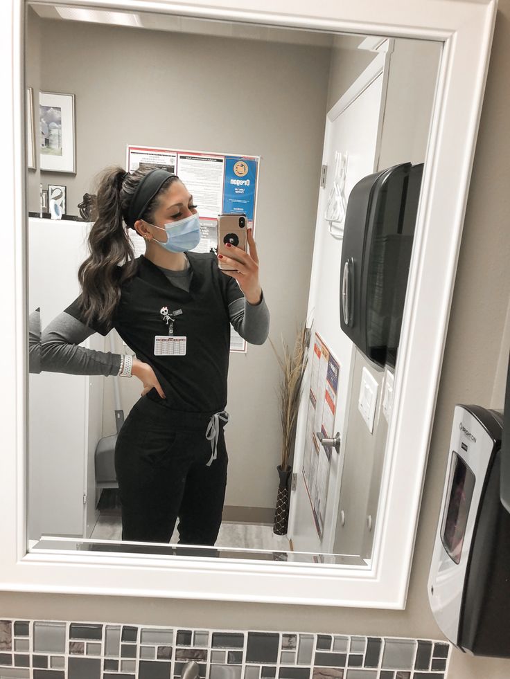 a woman taking a selfie in front of a bathroom mirror wearing a face mask